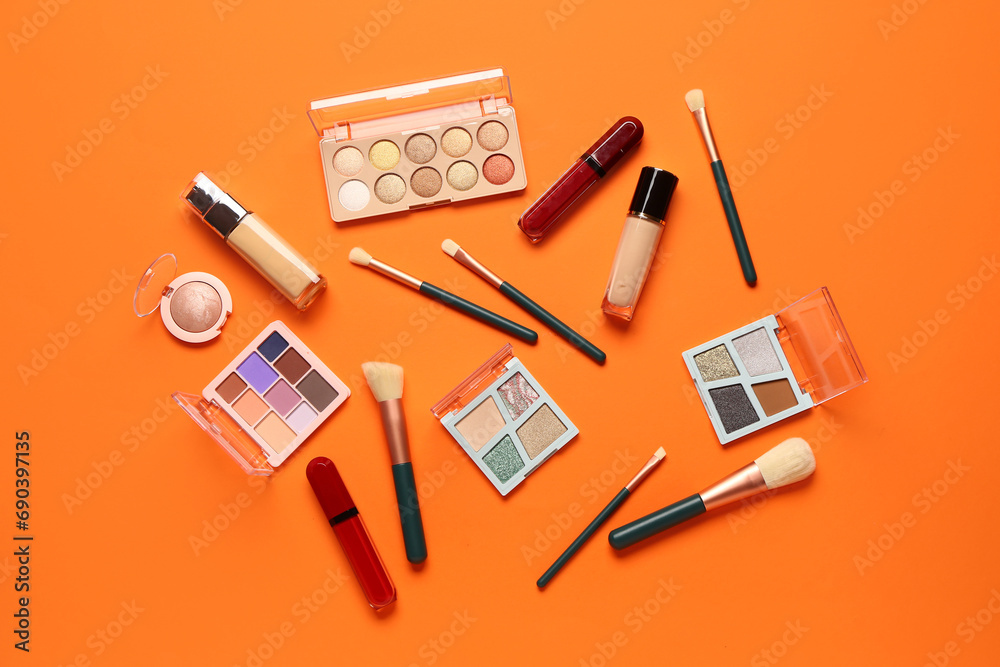 Beautiful palettes of eyeshadows and different decorative cosmetics on orange background