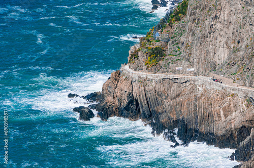 Front view, far distance of, a  narrow road cut, into rock wall, along, Arcidosso, coastline with sever wave action 