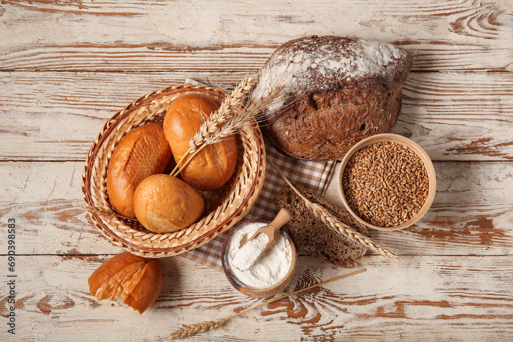 Loaves of different fresh bread with wheat spikelets and flour on white wooden background Loaves of different fresh bread with wheat spikelets and flour on white wooden background