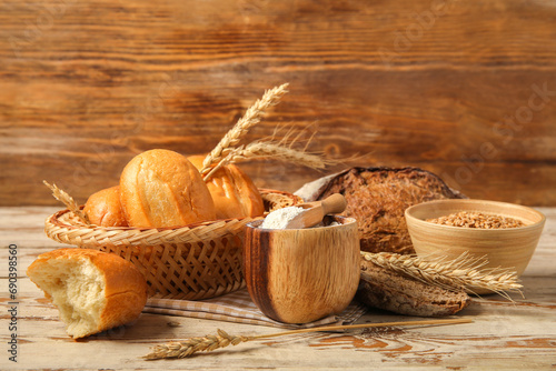 Loaves of different fresh bread with wheat spikelets and flour on wooden background