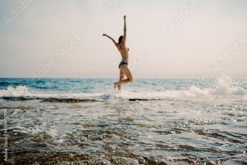 Capturing a moment of pure joy, a woman leaps against a backdrop of sparkling sea waves