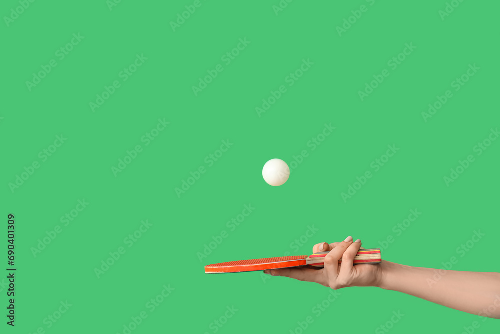 Female hand with ping pong racket tossing ball on green background Female hand with ping pong racket tossing ball on green background