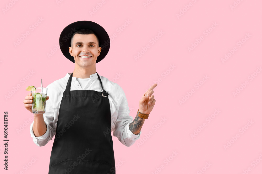 Young male bartender with glass of cocktail pointing at something on pink background Young male bartender with glass of cocktail pointing at something on pink background