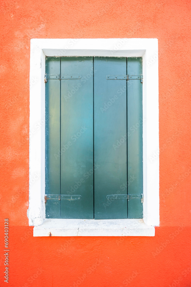 A windows with closed green shutters and a white frame on a bright red wall