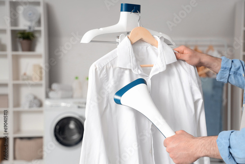 Quadro em tela Young man steaming clothes in laundry room, closeup