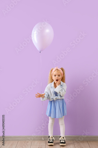 Cute shocked little girl with beautiful balloon near purple wall