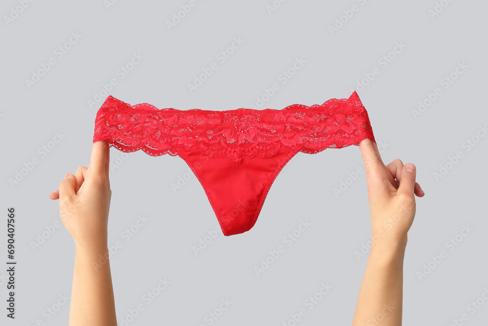 Female hands with sexy red panties on grey background, closeup - obrazy, fototapety, plakaty 