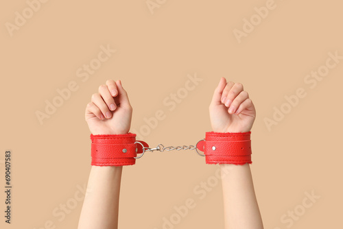 Female hands in red handcuffs from sex shop on color background, closeup