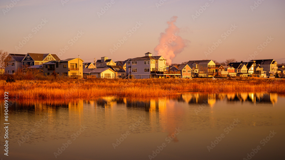 Peaceful coastal village landscape and water reflections at wintery sunrise with golden sunrays illuminating the reeds and sea grasses