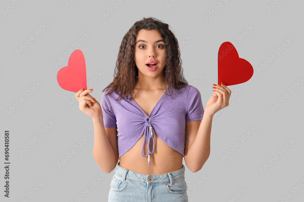 Shocked young woman with red paper hearts on grey background Shocked young woman with red paper hearts on grey background