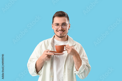 Young man in eyeglasses drinking coffee on blue background © Pixel-Shot