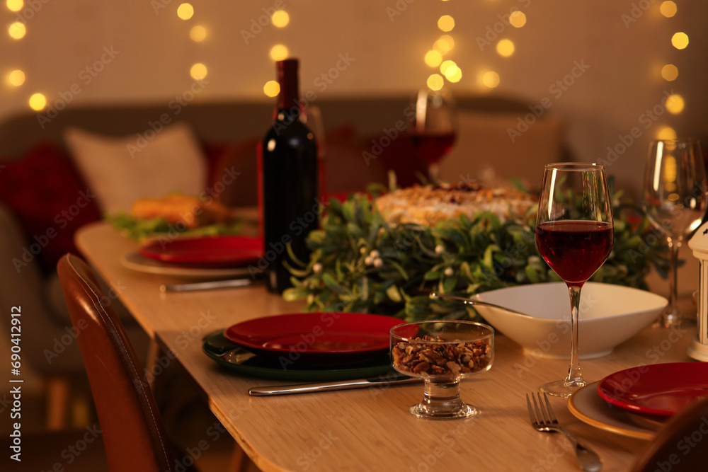 Christmas table setting with mistletoe wreath in room at night, closeup Christmas table setting with mistletoe wreath in room at night, closeup