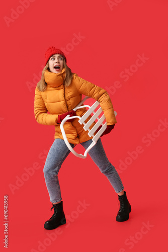 Beautiful young shocked woman in warm winter clothes with sledge on red background