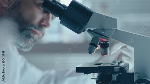 Senior male chemist pouring blood specimen microscope stage and examining it during research in laboratory photo