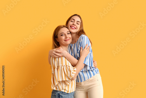 Happy young woman hugging her mother on yellow background. International Hug Day © Pixel-Shot