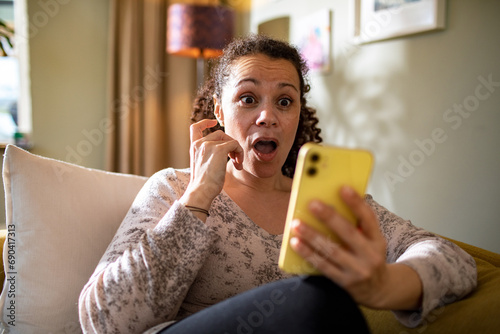Surprised Woman Reacting to Smartphone Content While Sitting on Couch photo