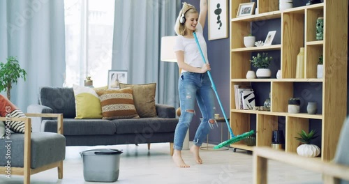 Cleaning, dancing and a woman with headphones for music in a house for fun energy and housework. Young female person in her apartment home with happiness, singing and joy to mop and clean floor photo