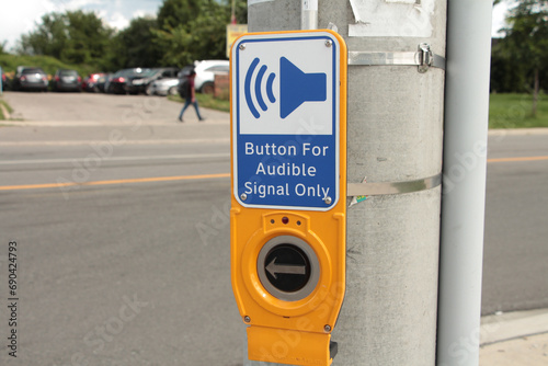 button for audible signal only crosswalk button with illustration of speaker making noise with road behind with pedestrian passing on sidewalk, speaker pointing at them, blue while yellow and black photo