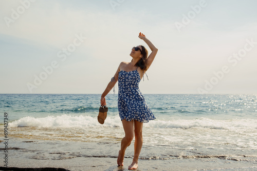 A moment of bliss as a woman in a summer dress savors the sun and sea, with sandals in hand