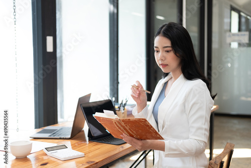 Portrait of a young beautiful Asian businesswoman holding a pencil and notebook, writing her work, she is thinking hard about her work.