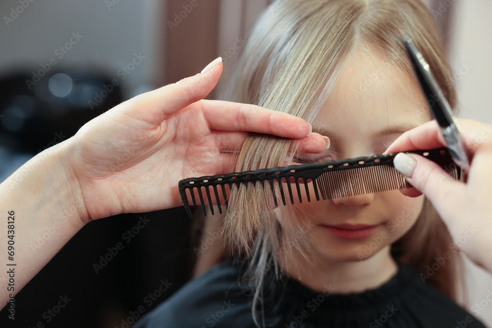 Obraz premium Professional hairdresser combing girl's hair in beauty salon, closeup