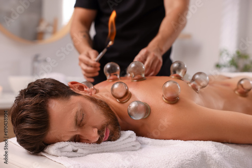 Φωτογραφία Therapist giving fire cupping treatment to patient on massage couch in spa salon