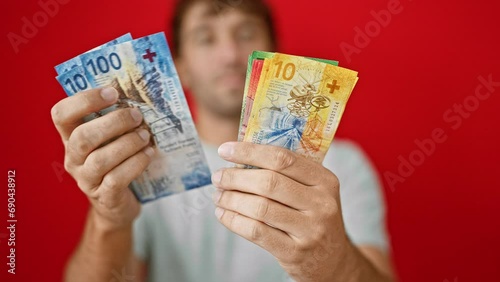 Young, blond, bearded, handsome man banking big, high-stakes counting swiss franc banknotes! isolated against a striking red background photo