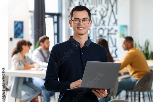 Team of employees working together in office. Happy man with laptop indoors