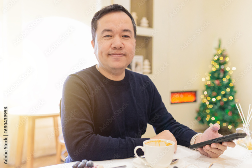 smart asian man wear glasses and holding ceramic cup with right hand, he do work and communicate with smartphone, he relax and drink hot latte coffee in cafe. Christmas seasonal smart asian man wear glasses and holding ceramic cup with right hand, he do work and communicate with smartphone, he relax and drink hot latte coffee in cafe. Christmas seasonal