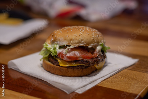 hamburguesa con queso, tomate y lechuga, sobre una servilleta blanca en un restaurante de comida rápida