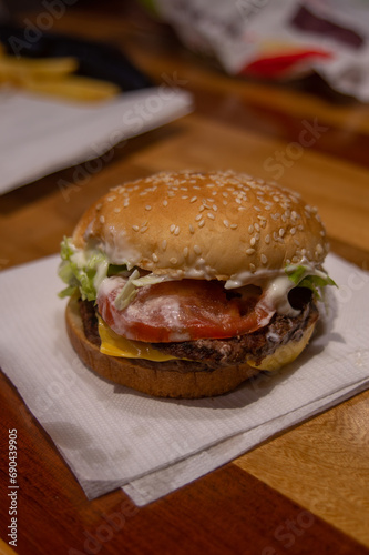hamburguesa con queso, tomate y lechuga, sobre una servilleta blanca en un restaurante de comida rápida en vertical