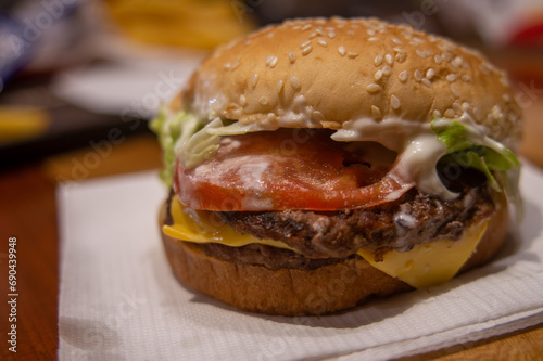 Toma cercana de una hamburguesa con queso, lechuga y tomate, sobre una servilleta blanca en un restaurante de comida rápida