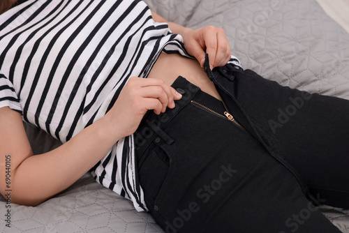 Woman trying to fit into her black jeans on bed, closeup