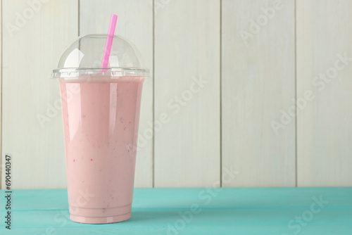 Tasty smoothie in plastic cup on light blue table against white wooden wall. Space for text