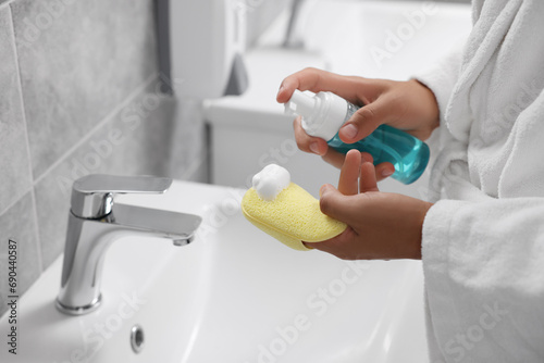 Fototapeta Naklejka Na Ścianę i Meble -  Young man applying face cleanser on sponge above sink in bathroom, closeup