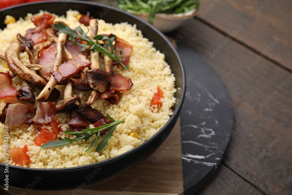 Tasty couscous with mushrooms and bacon in bowl on wooden table, closeup. Space for text Tasty couscous with mushrooms and bacon in bowl on wooden table, closeup. Space for text