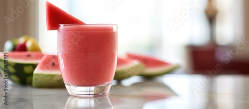 A glass cup filled with watermelon shake next to watermelon slices is served on a luxurious marble table