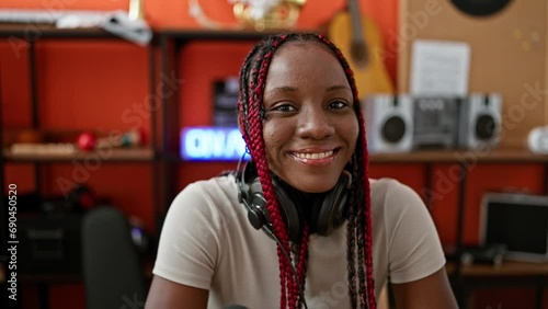 Smiling african american female musician wearing headphones, sitting at table in music studio, immersed in her beautiful sound photo