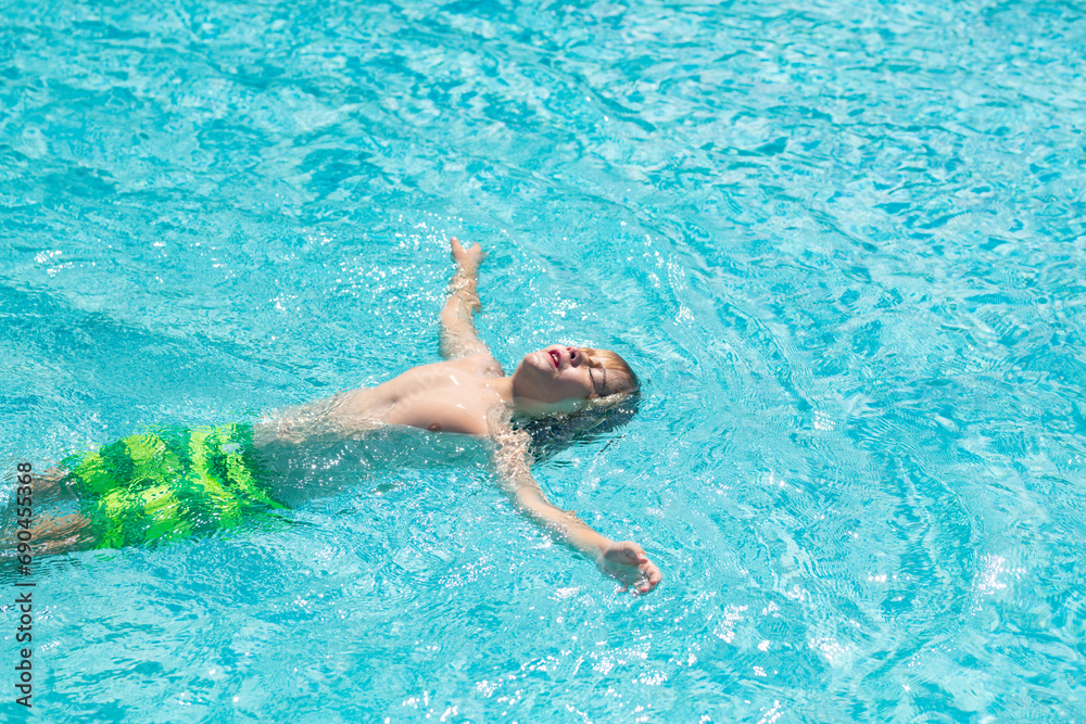 Excited child splashing water in pool. Little kid splashing in blue water of swimming pool. Cute boy swimming and splashing water with drops in pool. Child splashing and having fun in swim poolside.