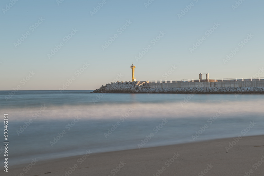 Beach scenery with a lighthouse and breakwater
