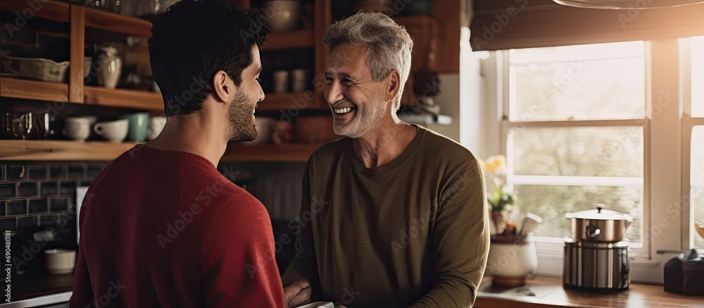 Youthful man brings coffee to older, joyful father in kitchen. Youthful man brings coffee to older, joyful father in kitchen.