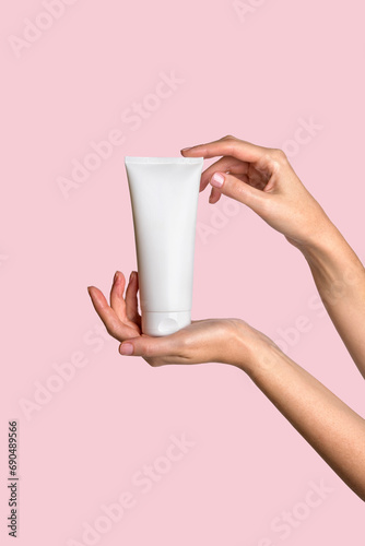 Woman hand showing cream product. Cosmetic product branding mockup. Daily skincare and body care routine. Female hand holding cosmetic product mockup on pink background