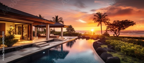 Sunset view of a tropical villa with garden, pool, and open living area.