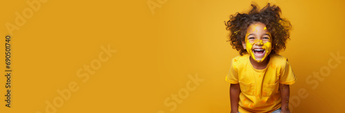 Happy African-American child with stained spotted t-shirt on yellow background looking into the camera with playful look. Advertisement horizontal banner with copy paste empty place for text photo