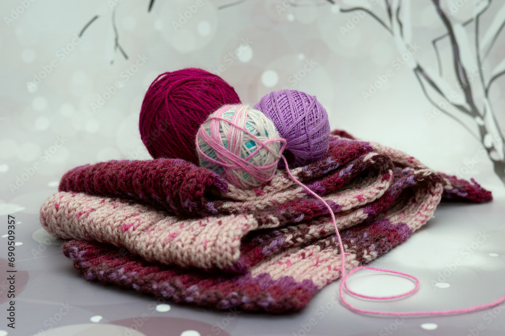 Fototapeta premium Knitted scarves and yarn on a winter background. Winter poster for interior. Knitted scarves symbolize the cold snowy season.