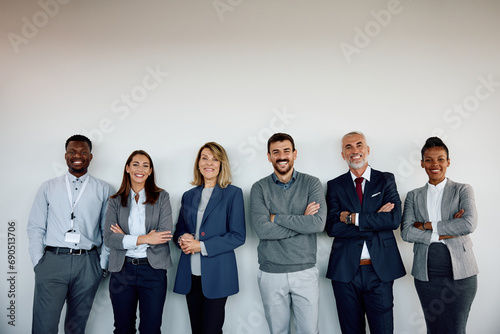 Mixed age group of happy business colleagues against wall looking at camera.
