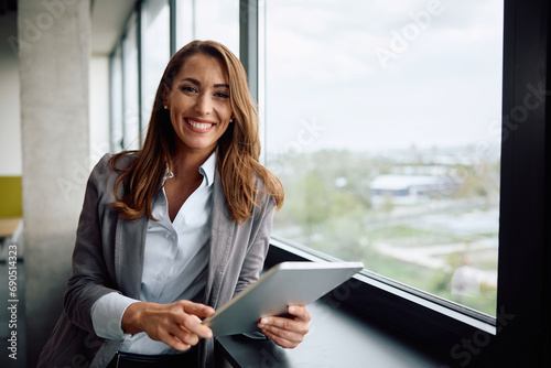 Young happy businesswoman using touchpad by window and looking at camera.