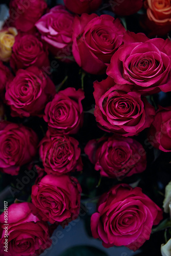 bouquet of pink roses in full bloom, with petals of a deep pink hue. The background is blurred, subtly revealing some orange roses