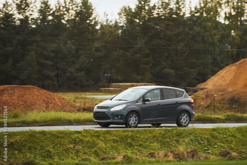 Driving fast on a road surrounded by greenery in a modern hatchback. Side view of modern hatchback moving on the highway.