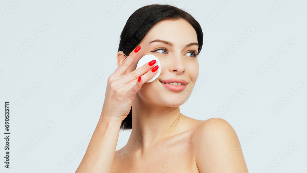 Charismatic, beautiful young woman using a cotton pad on a light isolated background. Concept of clean skin, facial care and natural cosmetics. Charismatic, beautiful young woman using a cotton pad on a light isolated background. Concept of clean skin, facial care and natural cosmetics.